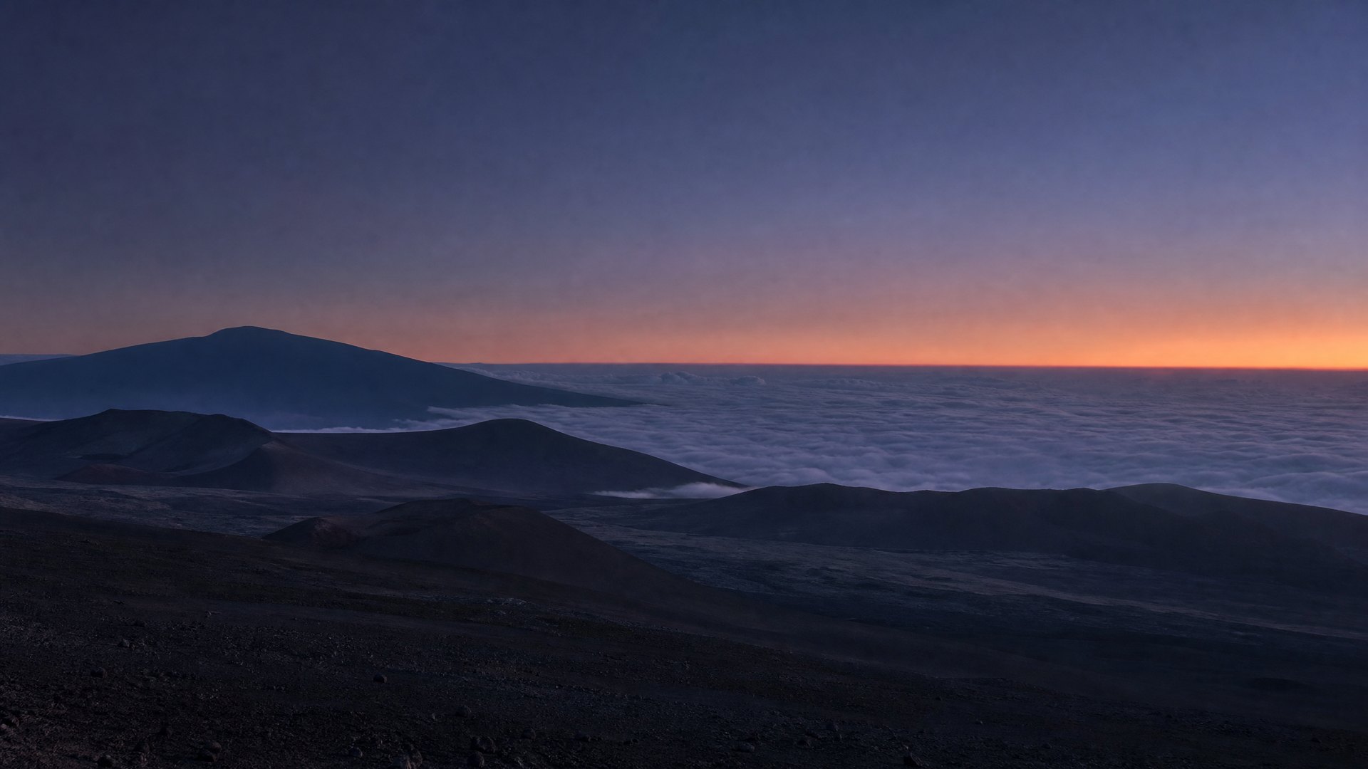 Mauna Kea volcanic ridgeline rising above a cloud layer during blue hour