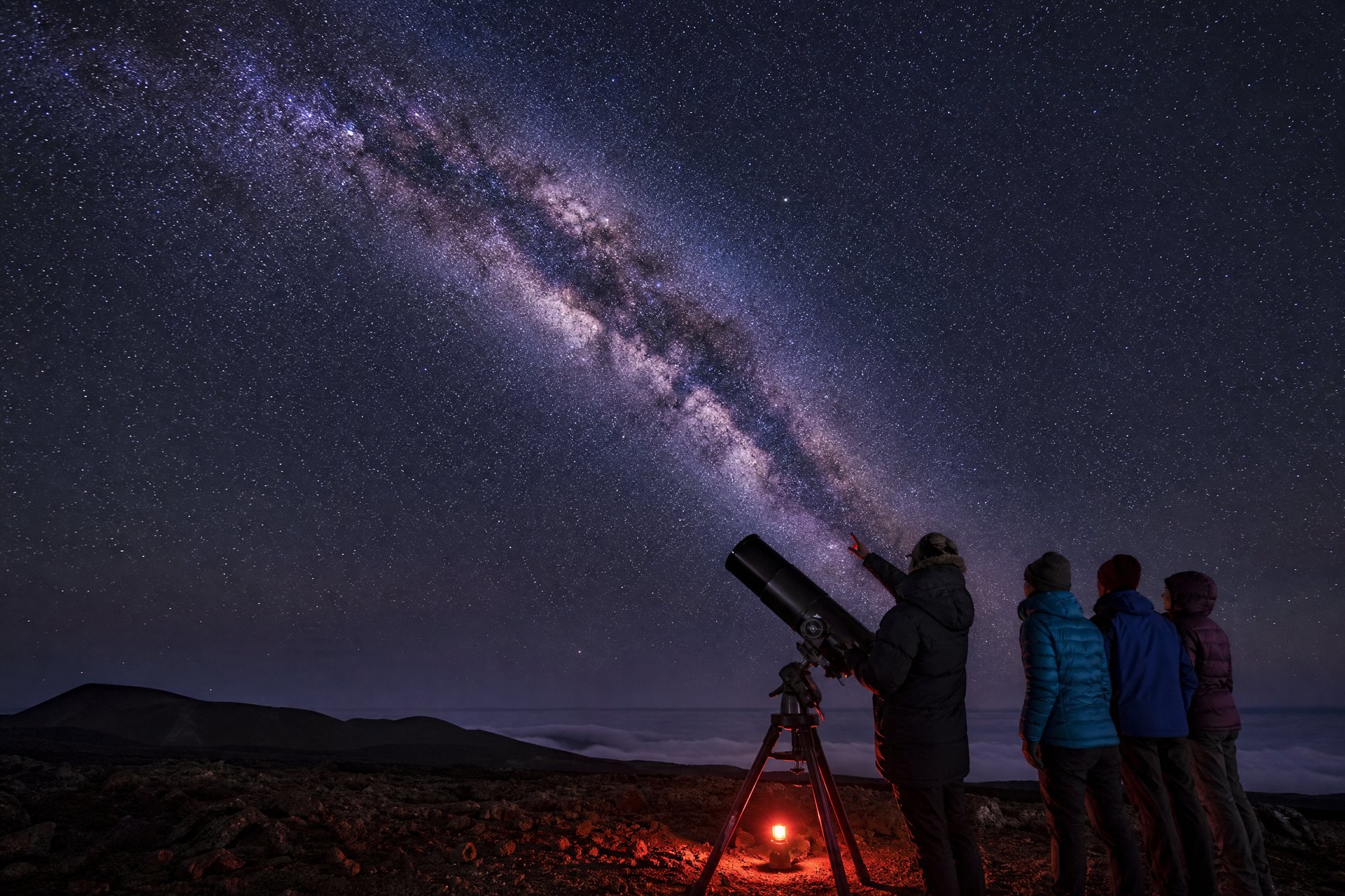 Guide using a portable telescope with guests on a dark Mauna Kea lava plateau